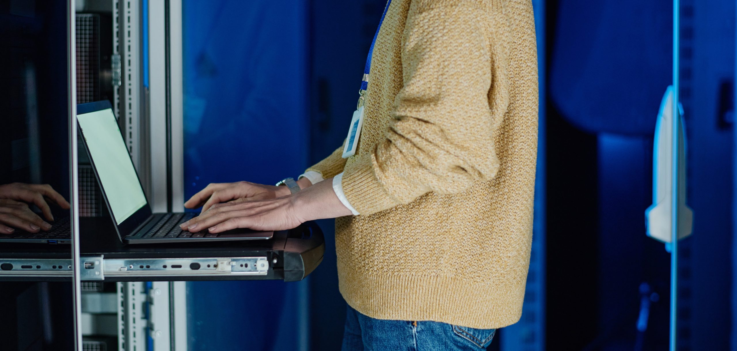 Close-up of female engineer typing on laptop to load data from server computer during her work in data center